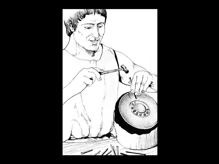 Artigiano in atto di eseguire la decorazione a cesello di un vaso di metallo.